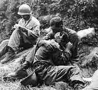 a soldier comforts another who just lost his buddy in a fire firght while a corpman nearby fills out death certificats